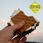 Sweet and playfully gooey. The outdoorsy classic constructed of melted marshmallow, chocolate and graham crackers reimagined for your coffee cup; image of hand holding a S'more